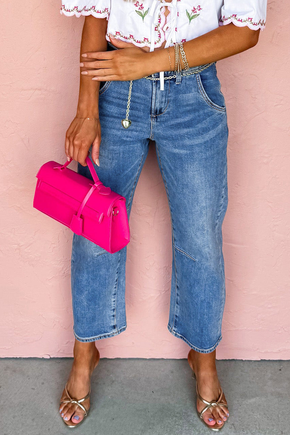Person wearing a white blouse with floral patterns and blue jeans, holding a pink handbag against a pink background.