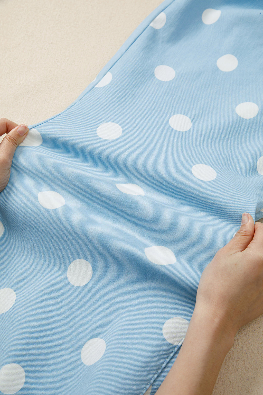 Blue jeans with white polka dots held by hands stretched on a light background