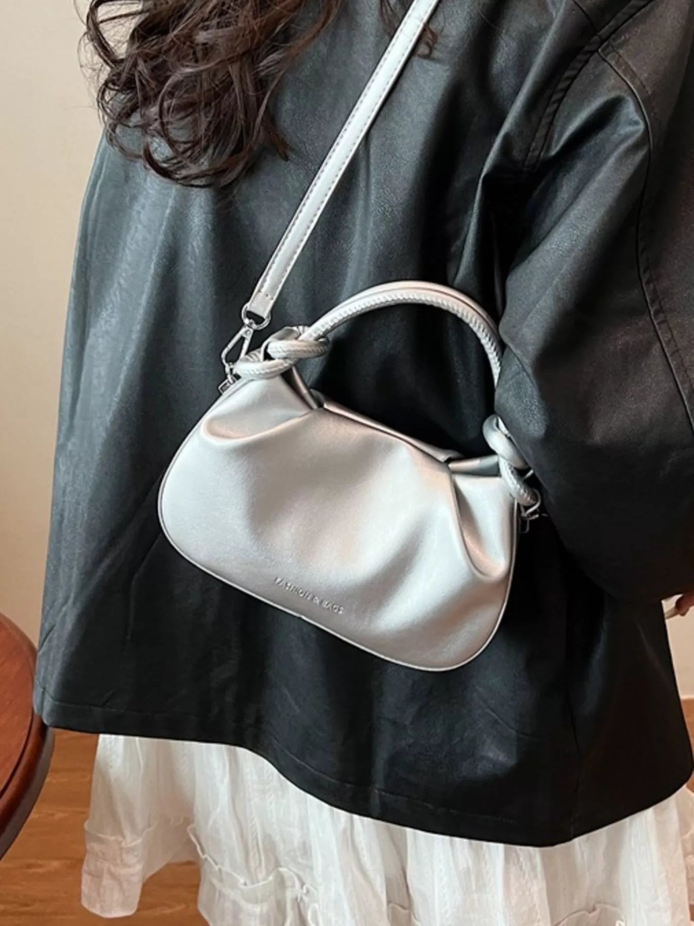Person wearing a silver handbag with a visible brand logo.