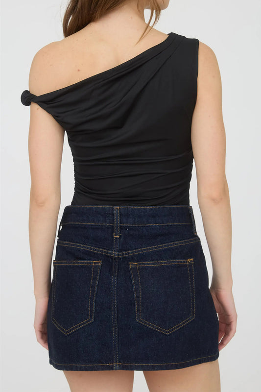 Person wearing a black one-shoulder top and blue denim skirt on a white background back view