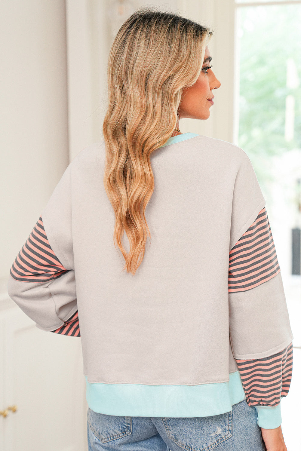 Woman wearing a light gray sweatshirt with striped sleeves in a casual setting