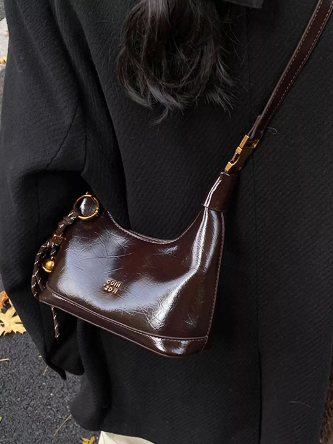 Brown leather handbag with gold accents worn by a person in a black coat.