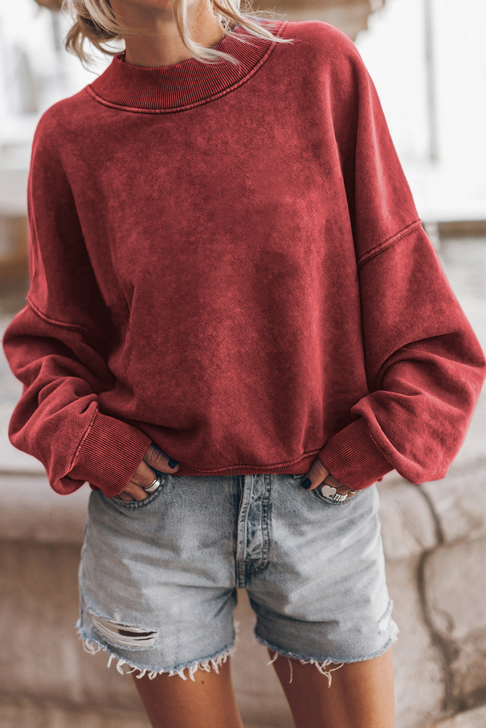 Person wearing a red sweatshirt and denim shorts indoors