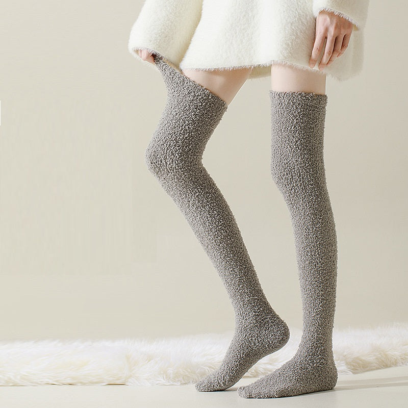 Person wearing gray fuzzy knee-high socks with a white coat on a light background