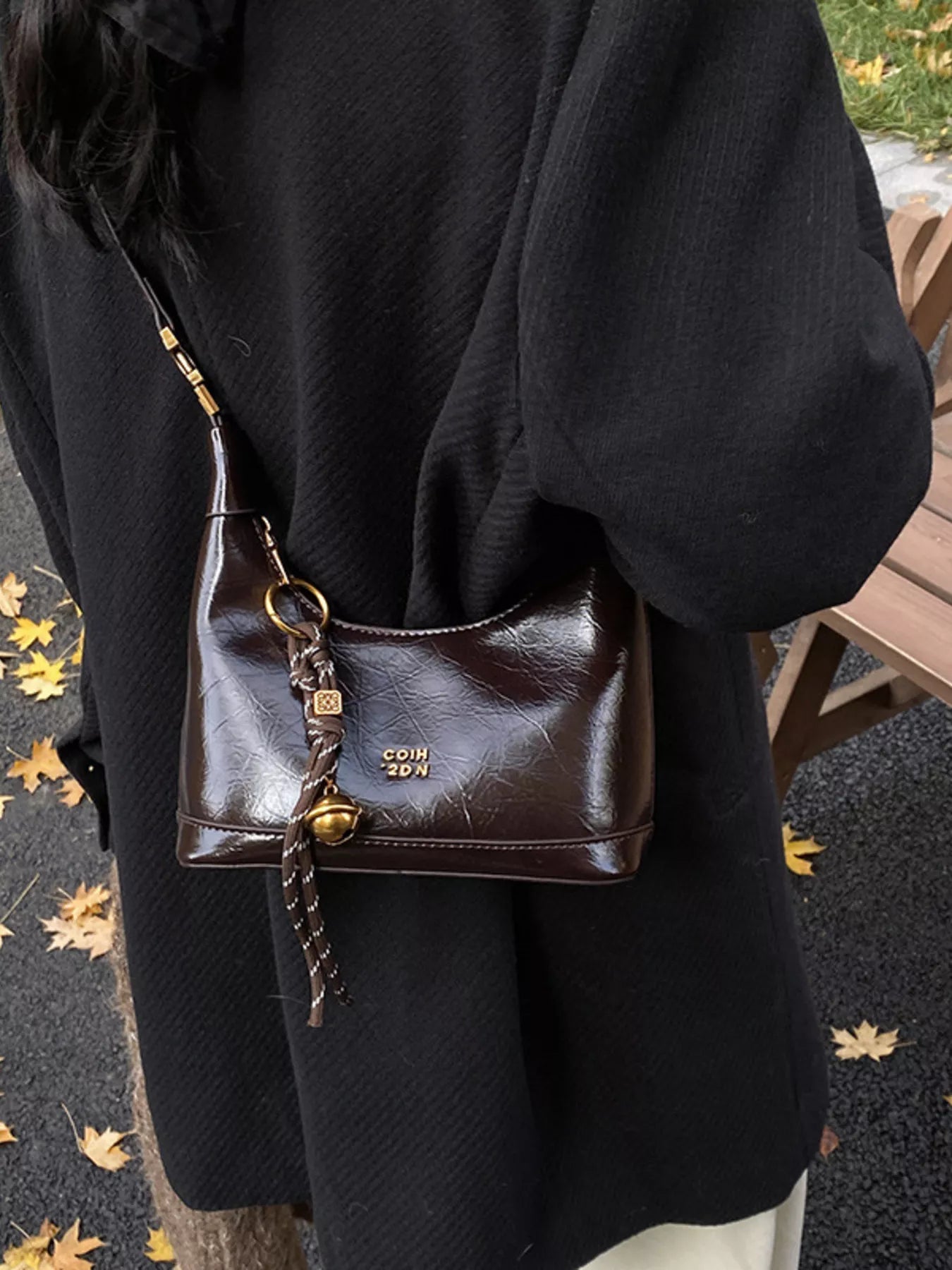 Brown leather handbag with gold accents worn over a black coat