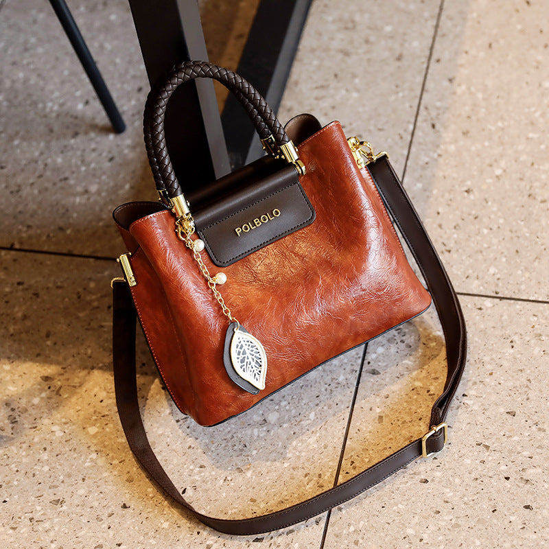 Brown handbag with black handle and strap on a textured surface