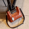 Brown handbag with black handle and strap on a textured surface