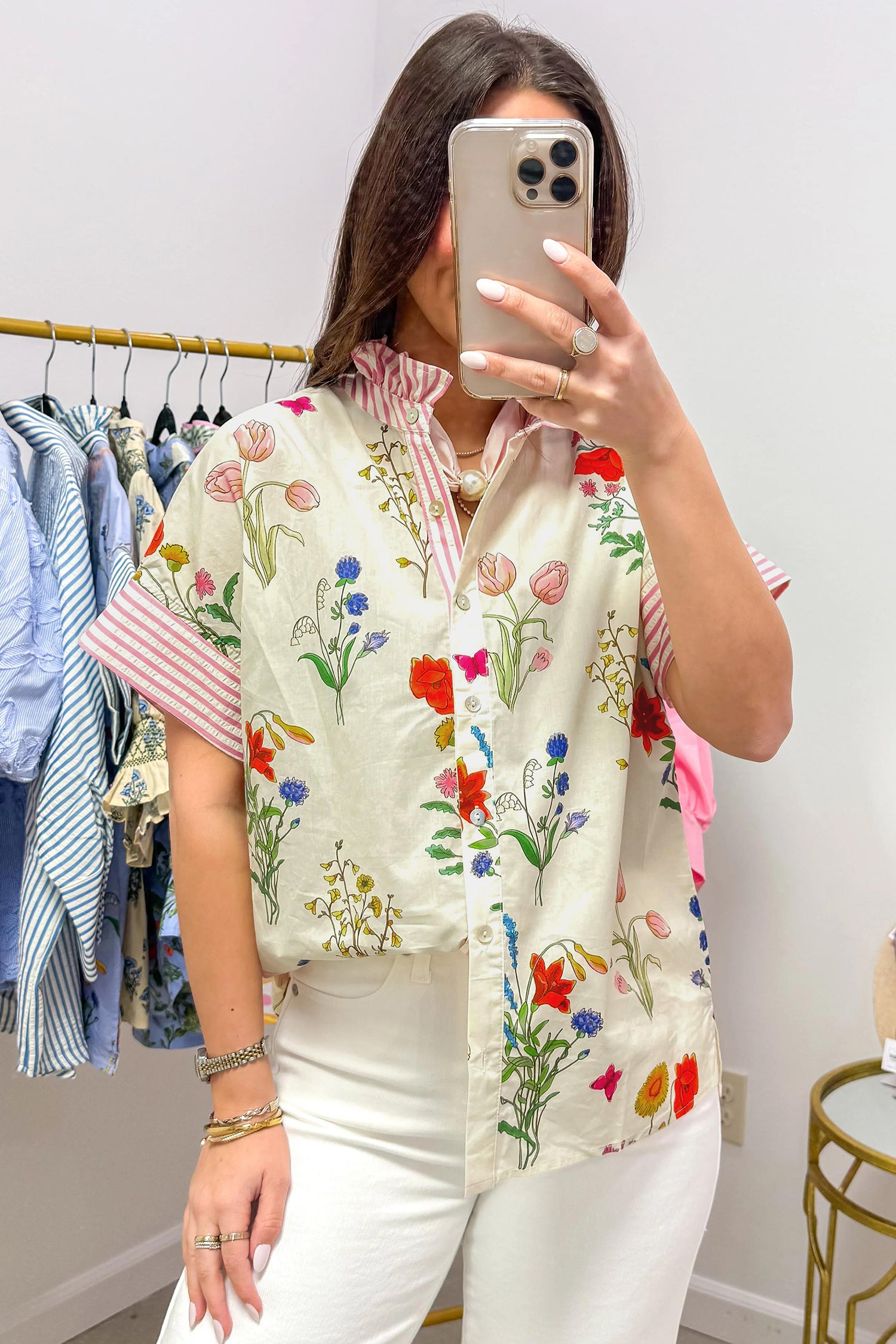 Woman taking a mirror selfie wearing a floral embroidered shirt in a clothing store.