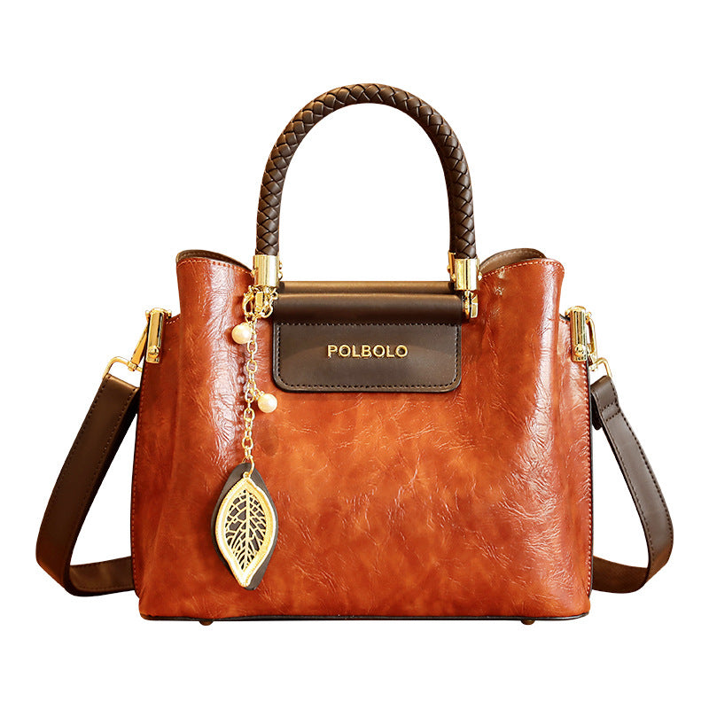 Brown handbag with braided handle and decorative leaf charm on a white background