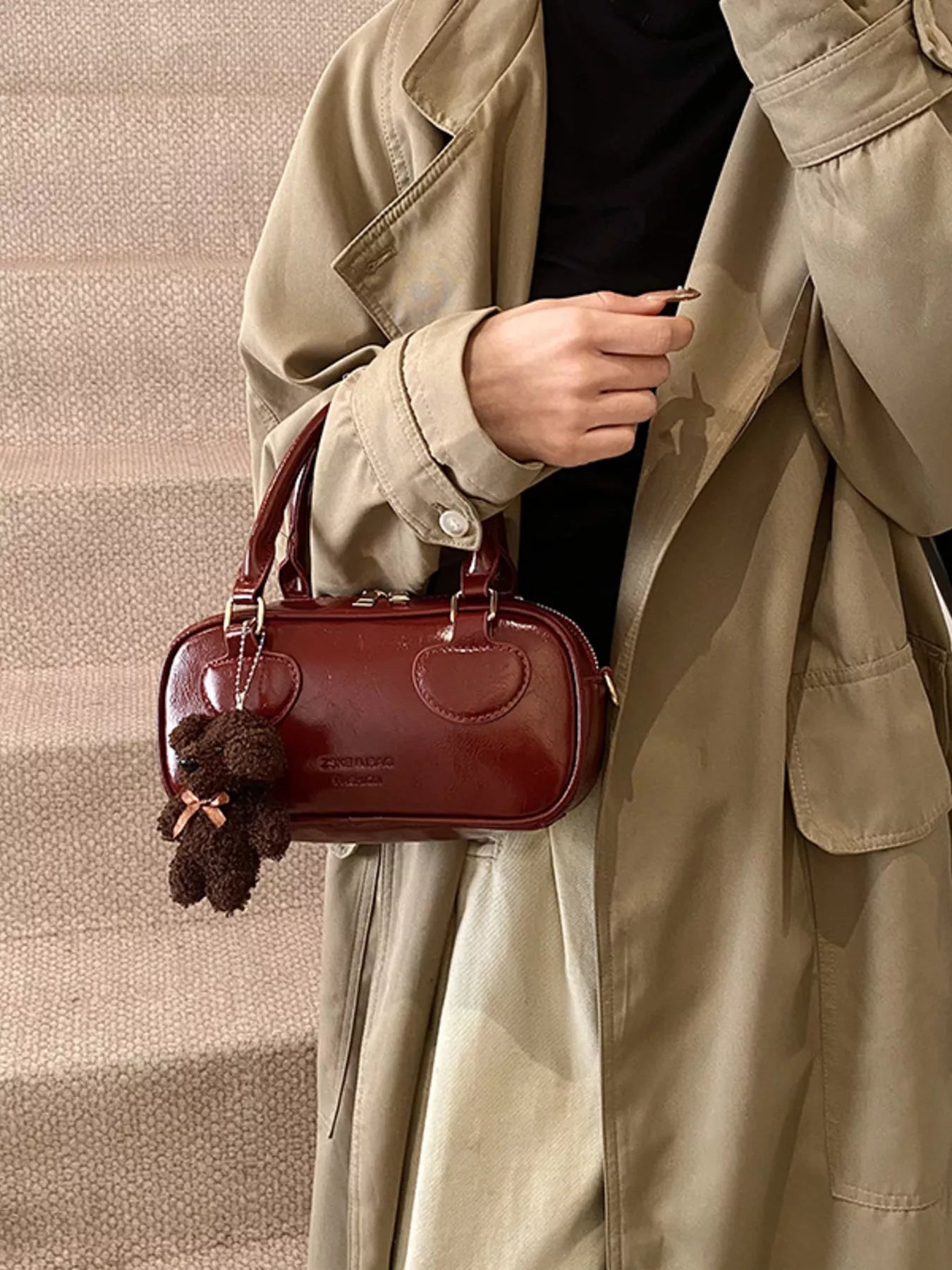 Person holding a red handbag with a decorative bow, wearing a beige trench coat.