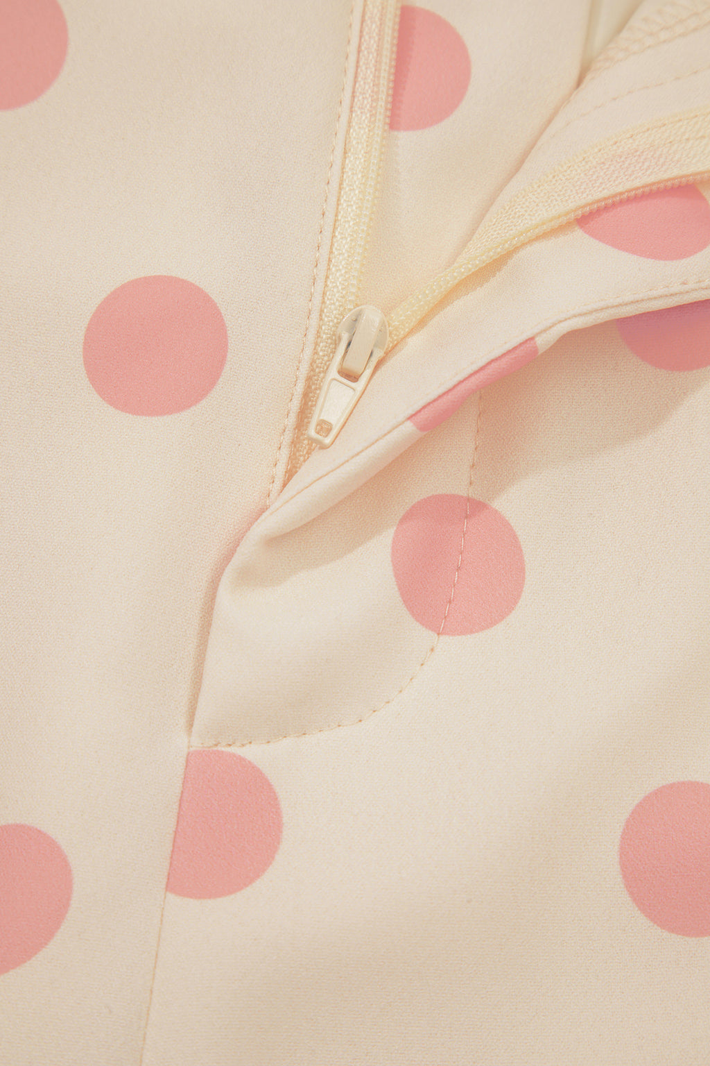 Close-up of a beige fabric with pink polka dots and a zipper.