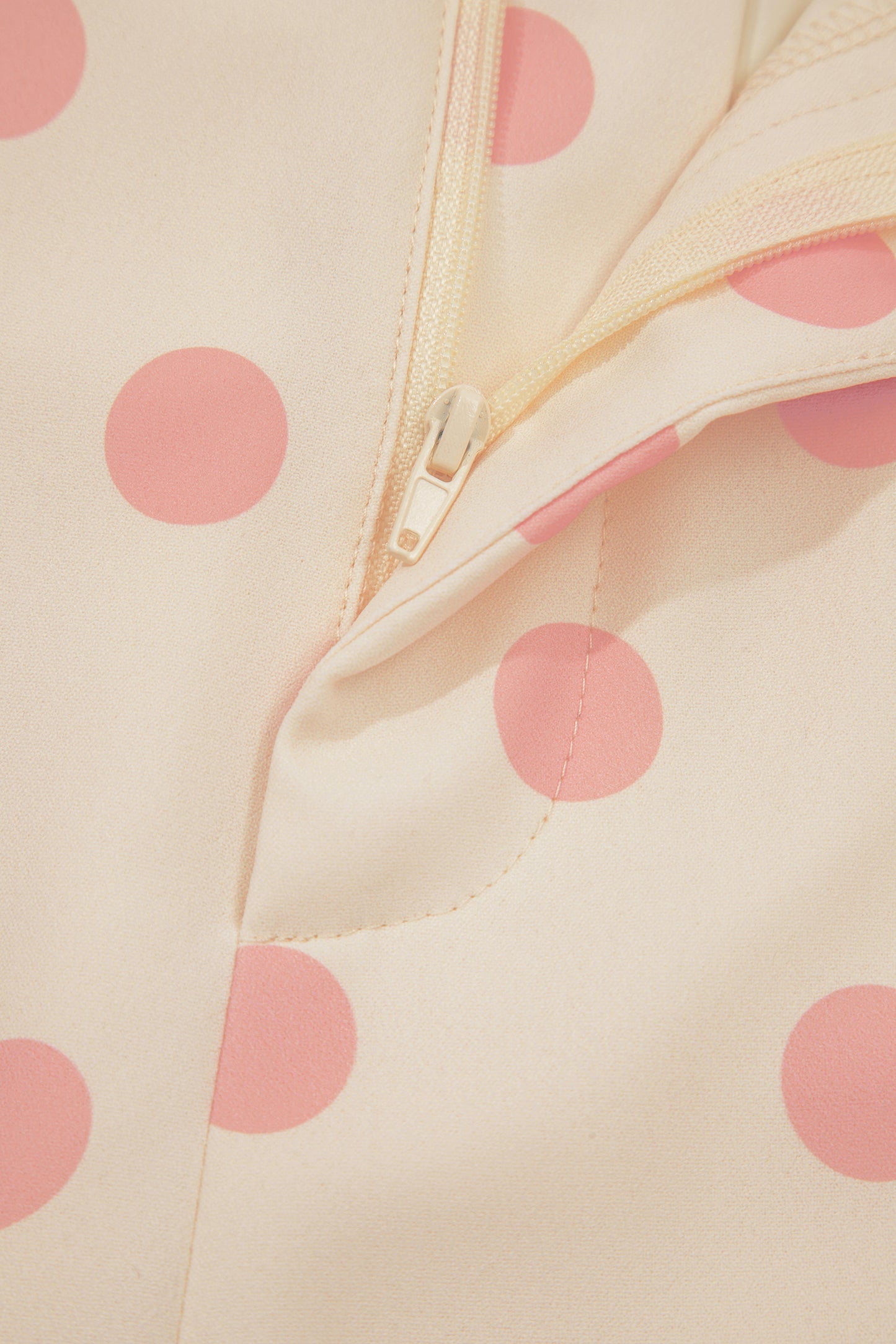 Close-up of a beige fabric with pink polka dots and a zipper.