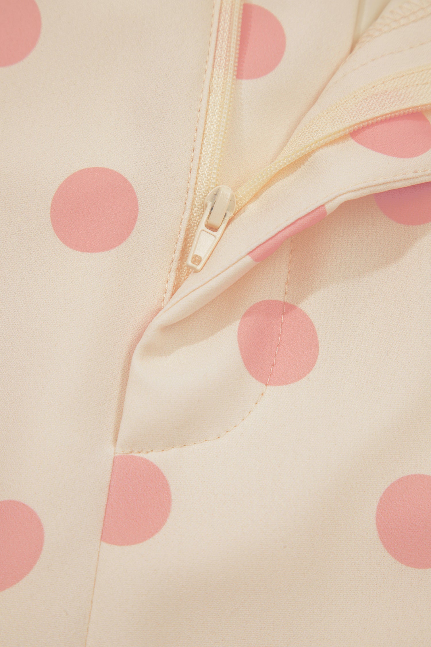 Close-up of a beige fabric with pink polka dots and a zipper.