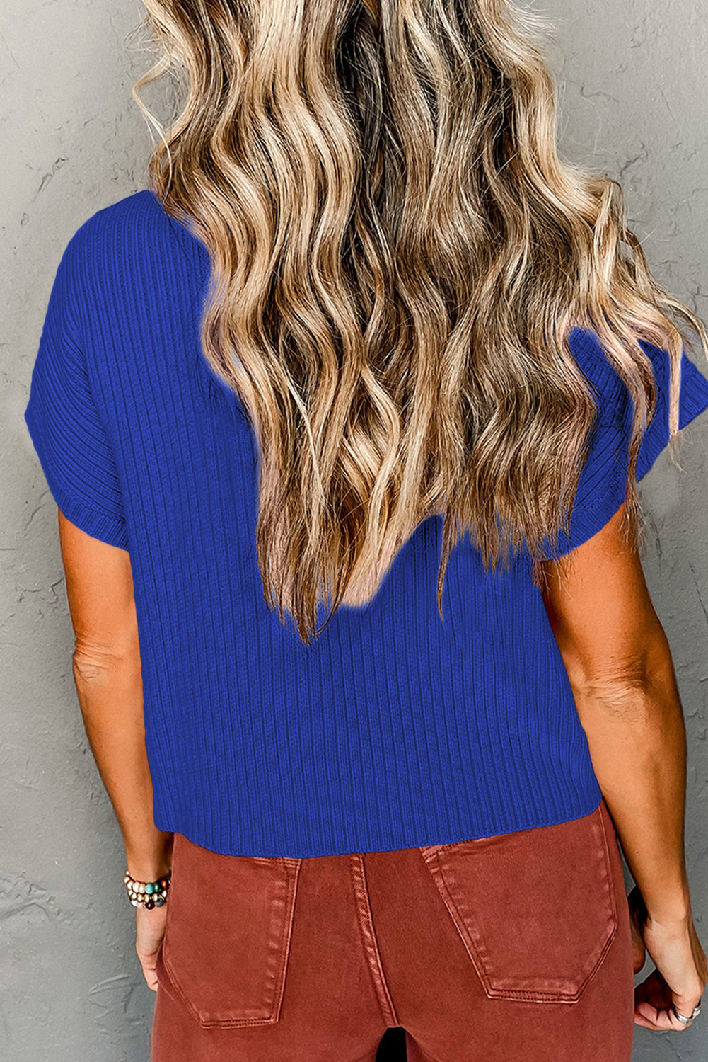 Person wearing a blue top and brown pants against a gray background