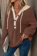 Woman wearing a brown and beige sweater with blue jeans, standing against a neutral background.