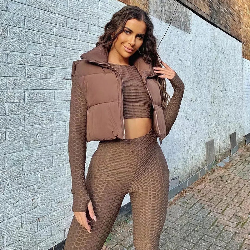 Woman in brown outfit standing against a light gray brick wall.