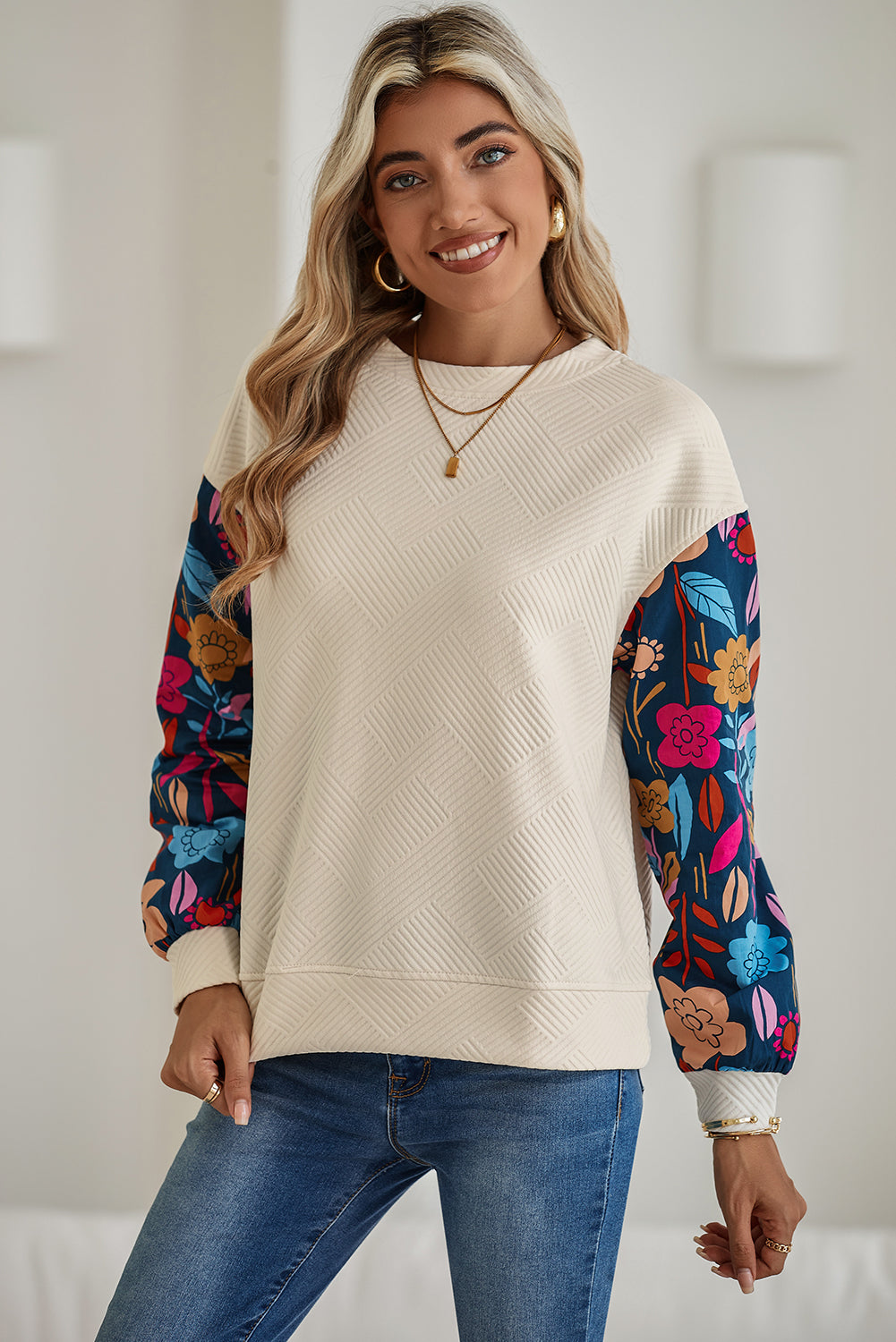 Woman wearing a cream sweater with floral sleeves against a white background