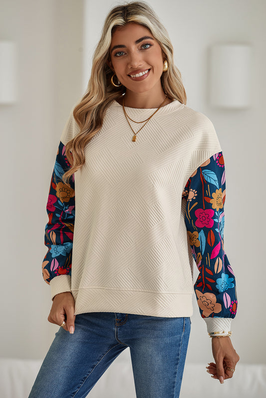 Woman wearing a cream sweater with floral sleeves against a white background