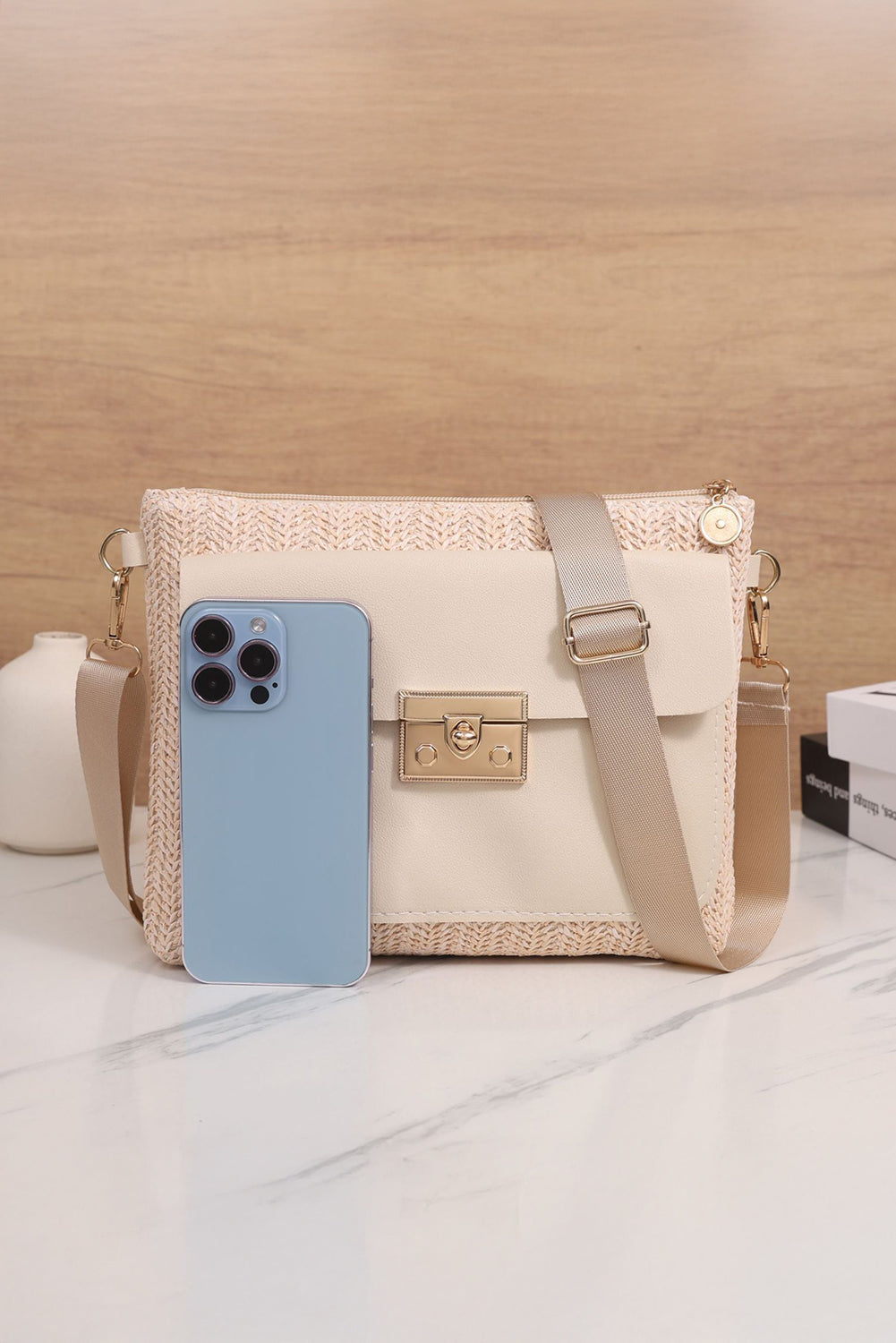 White woven handbag with gold accents on a light surface size comparison to a phone