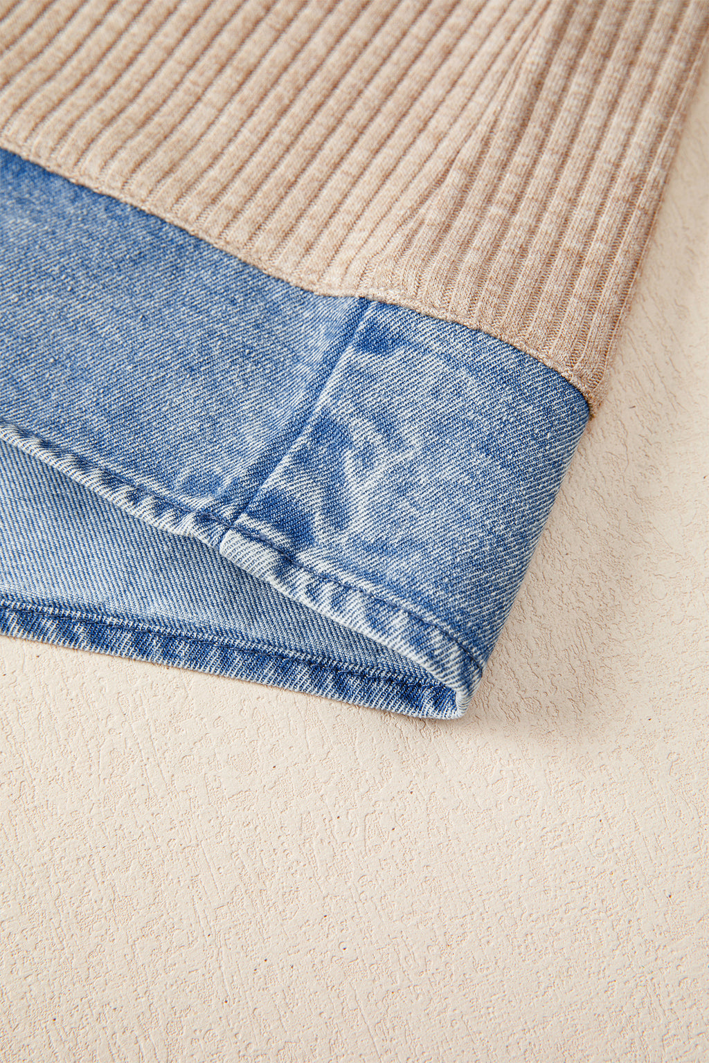 Close-up of a beige corduroy blouse with blue denim trim on a neutral background