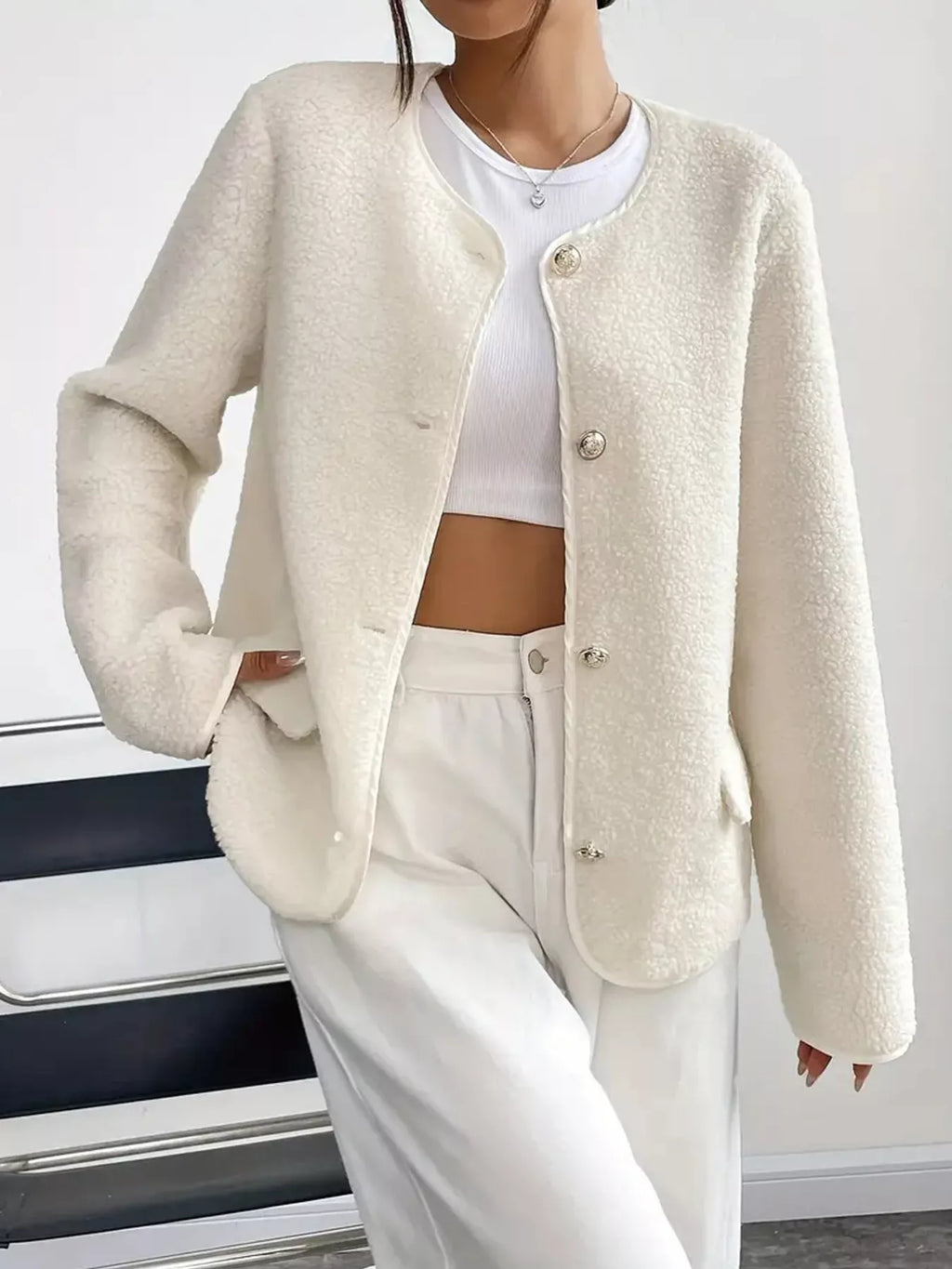 Person wearing a cream-colored cardigan over a white top and pants on a neutral background