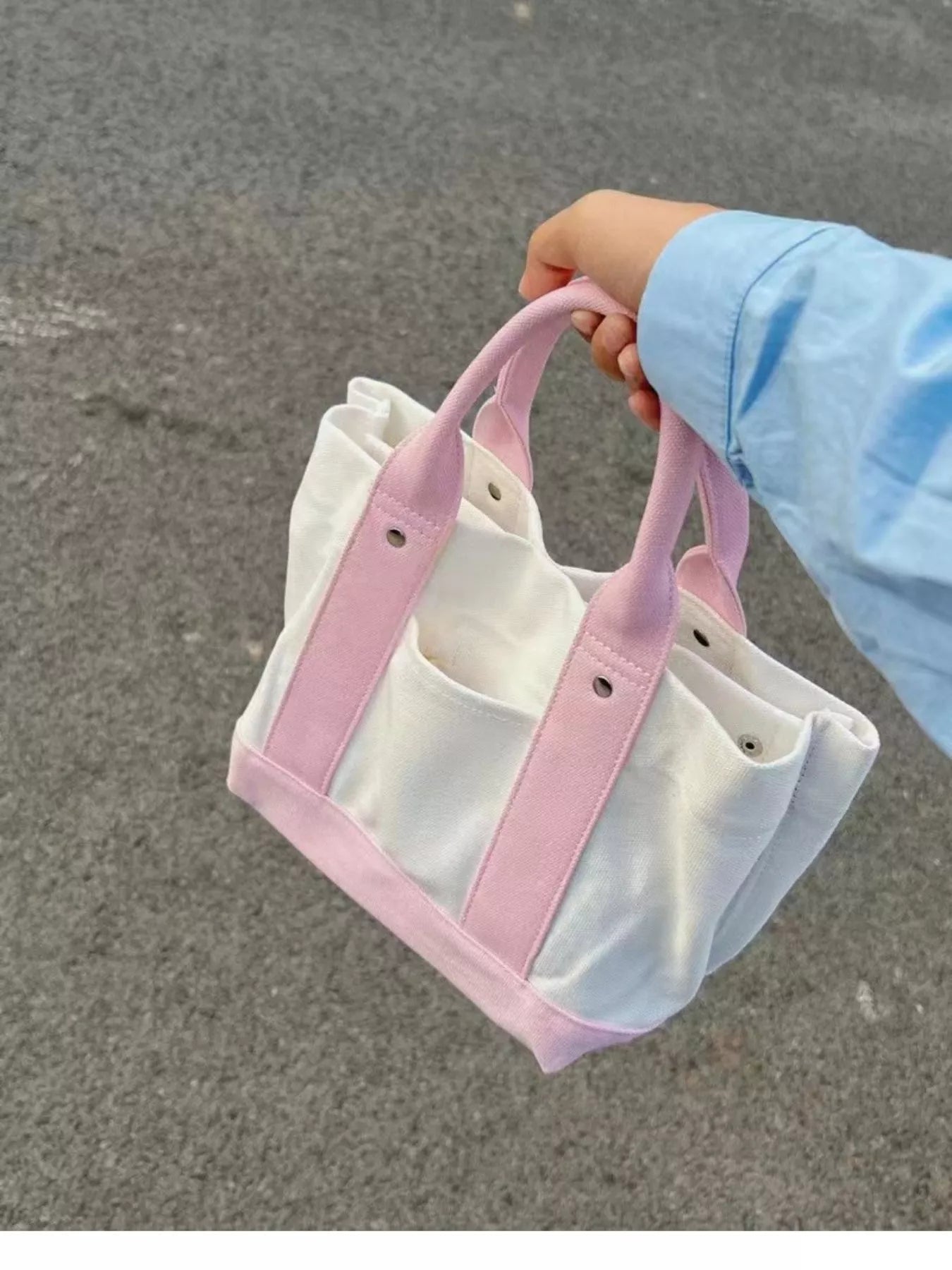 White tote bag with pink handles held by a person on a gray pavement.