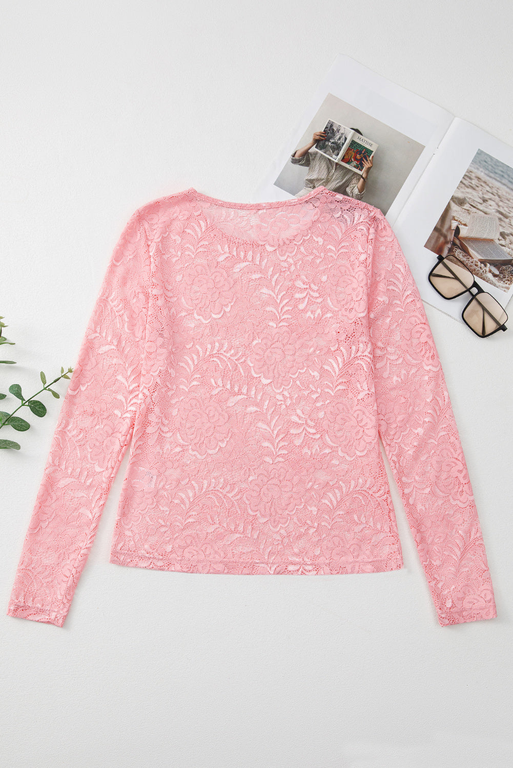 Pink lace top on a white surface with sunglasses and a plant