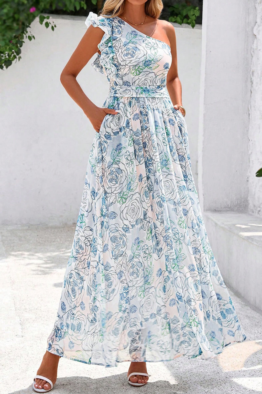 Woman wearing a floral one-shoulder dress against a white wall. Side view
