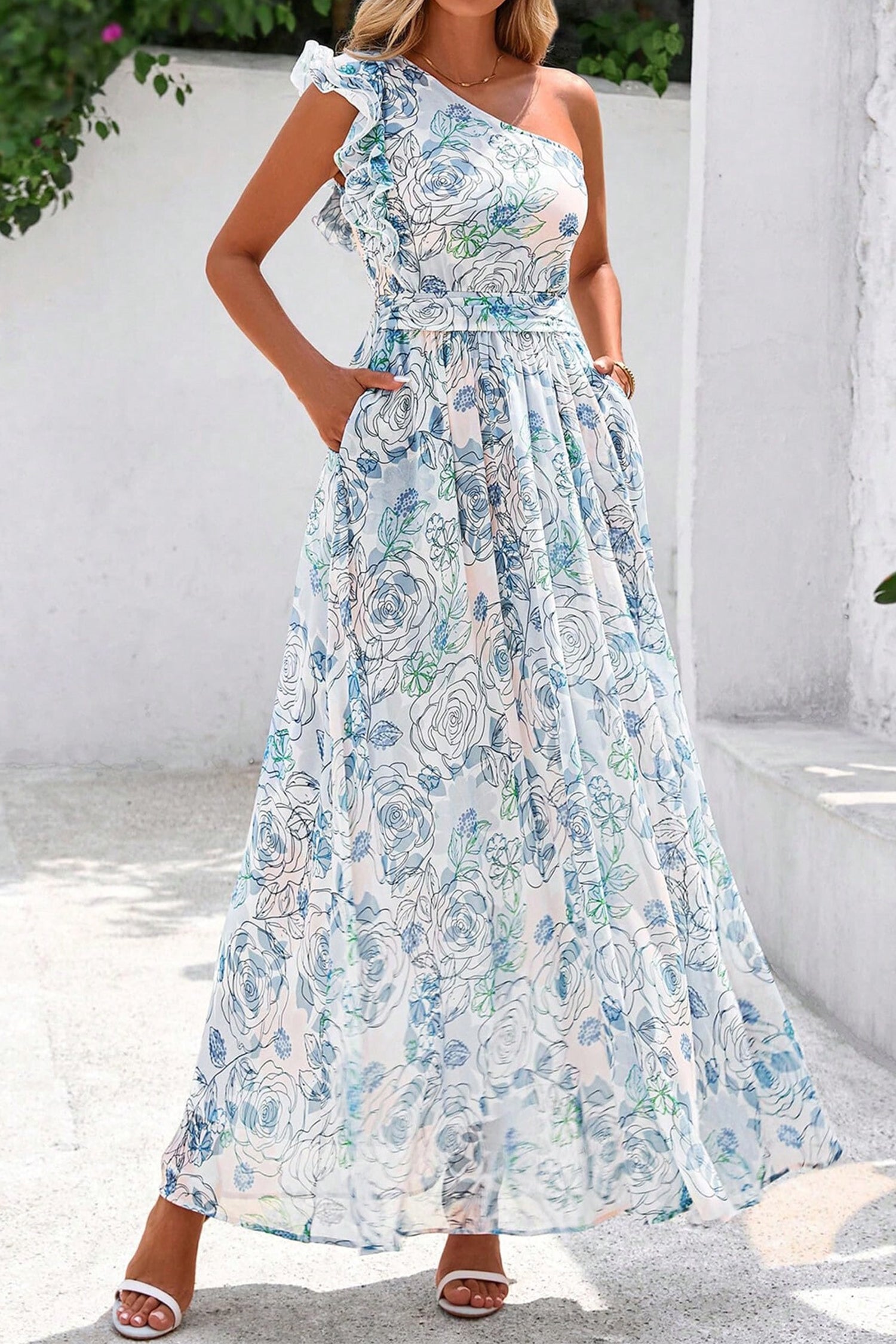 Woman wearing a floral one-shoulder dress against a white wall. Side view