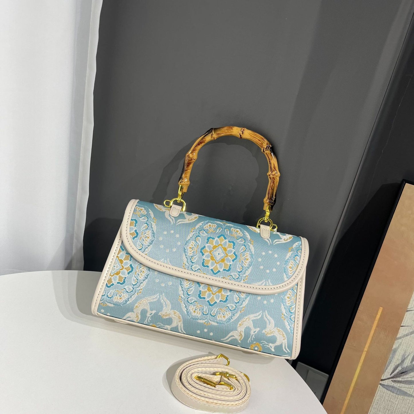 Blue patterned handbag with gold handle and strap on a white surface