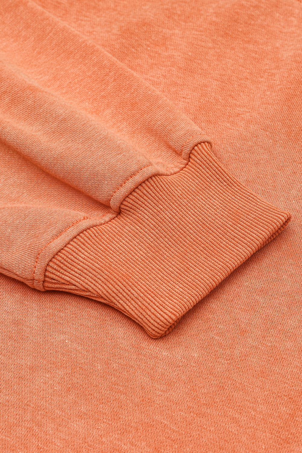 Close-up of a peach-colored sweater with ribbed cuffs and hem.