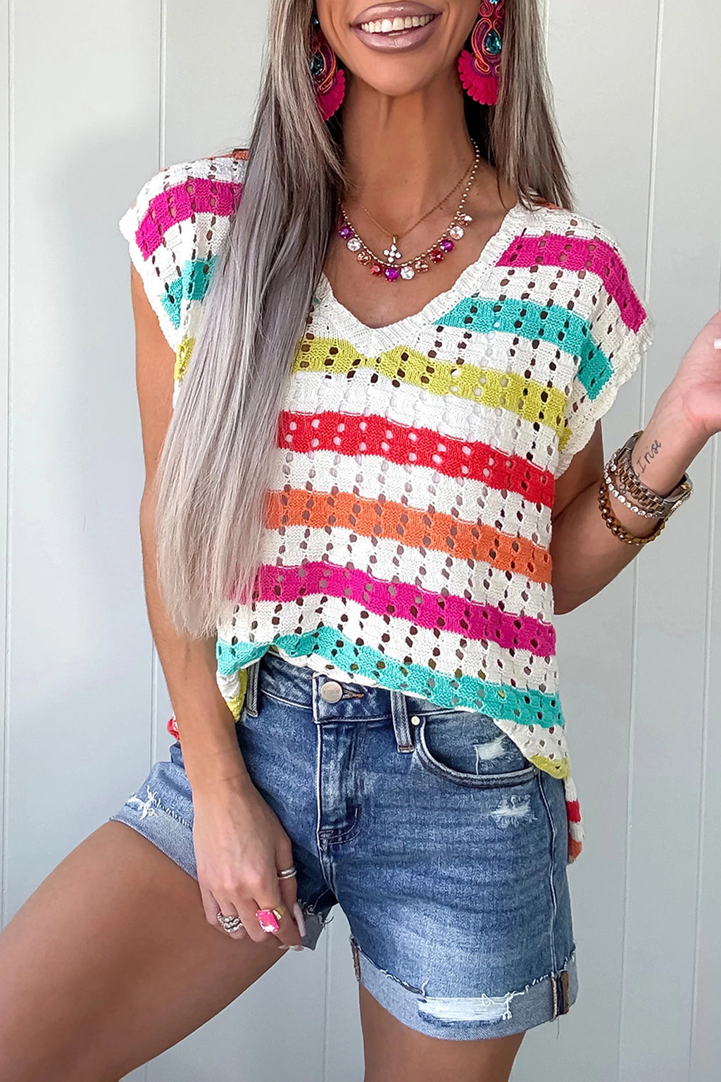 Woman wearing a colorful striped sleeveless top and denim shorts against a white background