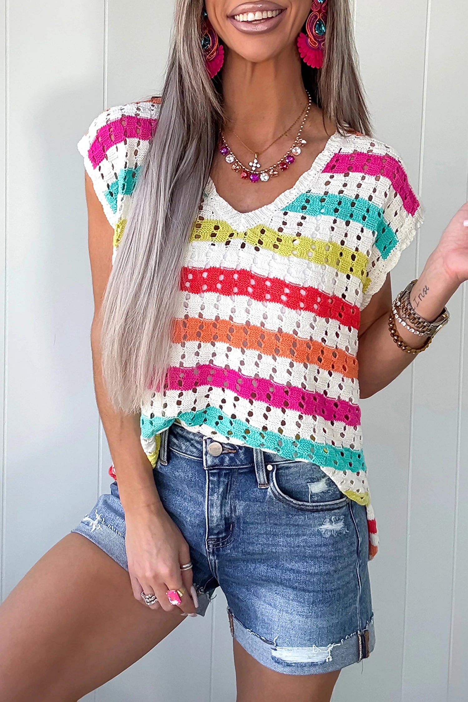 Woman wearing a colorful striped sleeveless top and denim shorts against a white background