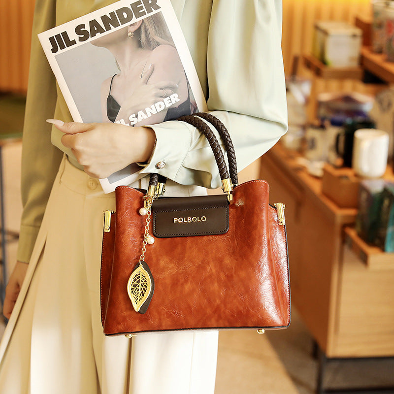 Person holding a brown handbag with a magazine titled 'Jil Sander' in an indoor setting.