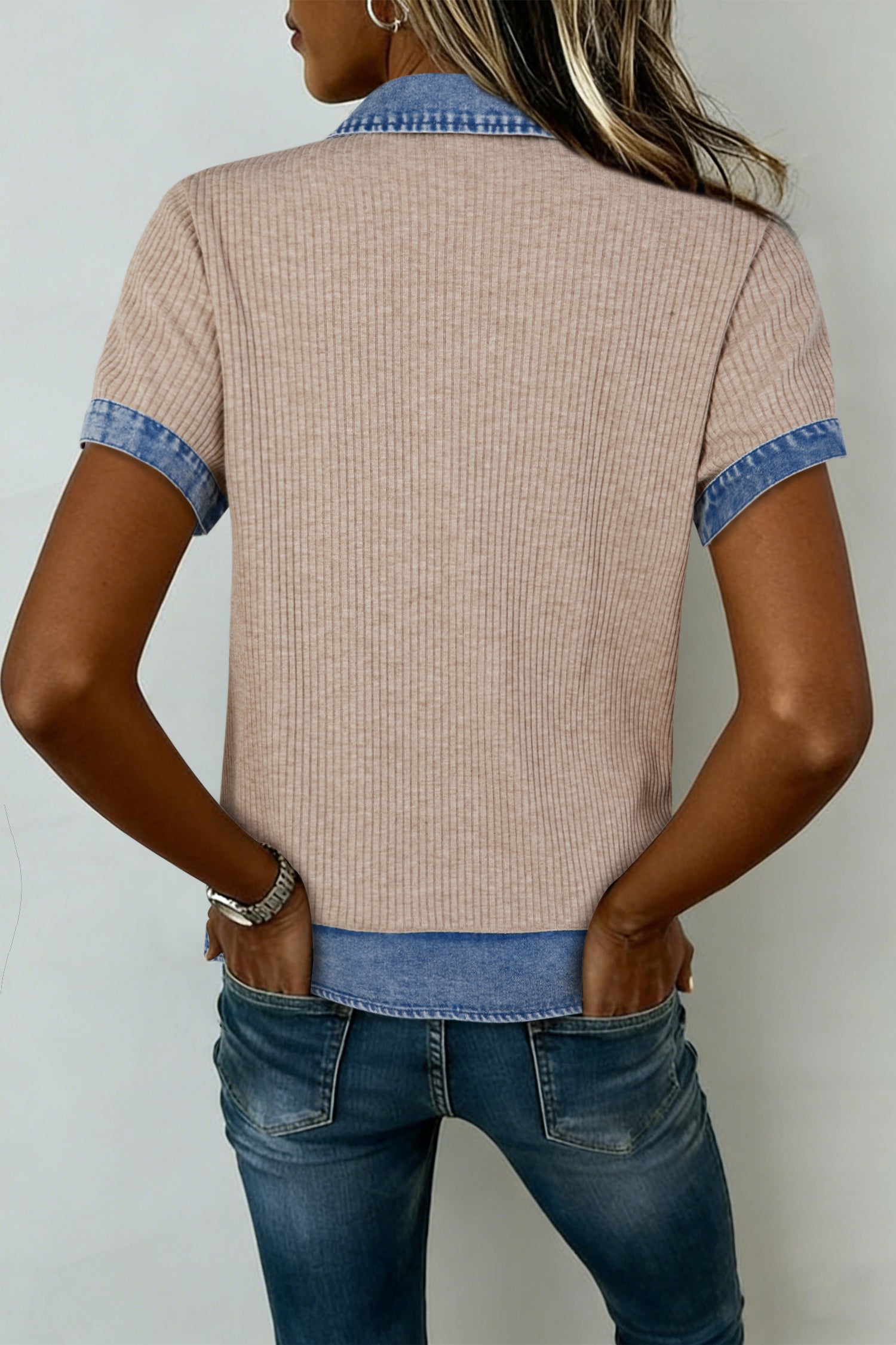 Person wearing a beige short-sleeve shirt with blue trim and blue jeans against a white background back view