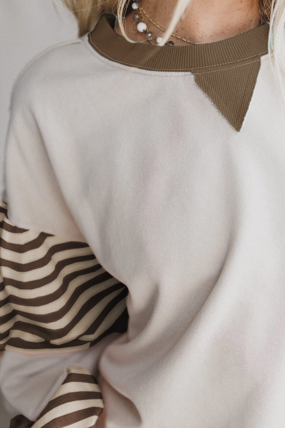 Close-up of a person wearing a white sweater with brown and black patterned sleeves.
