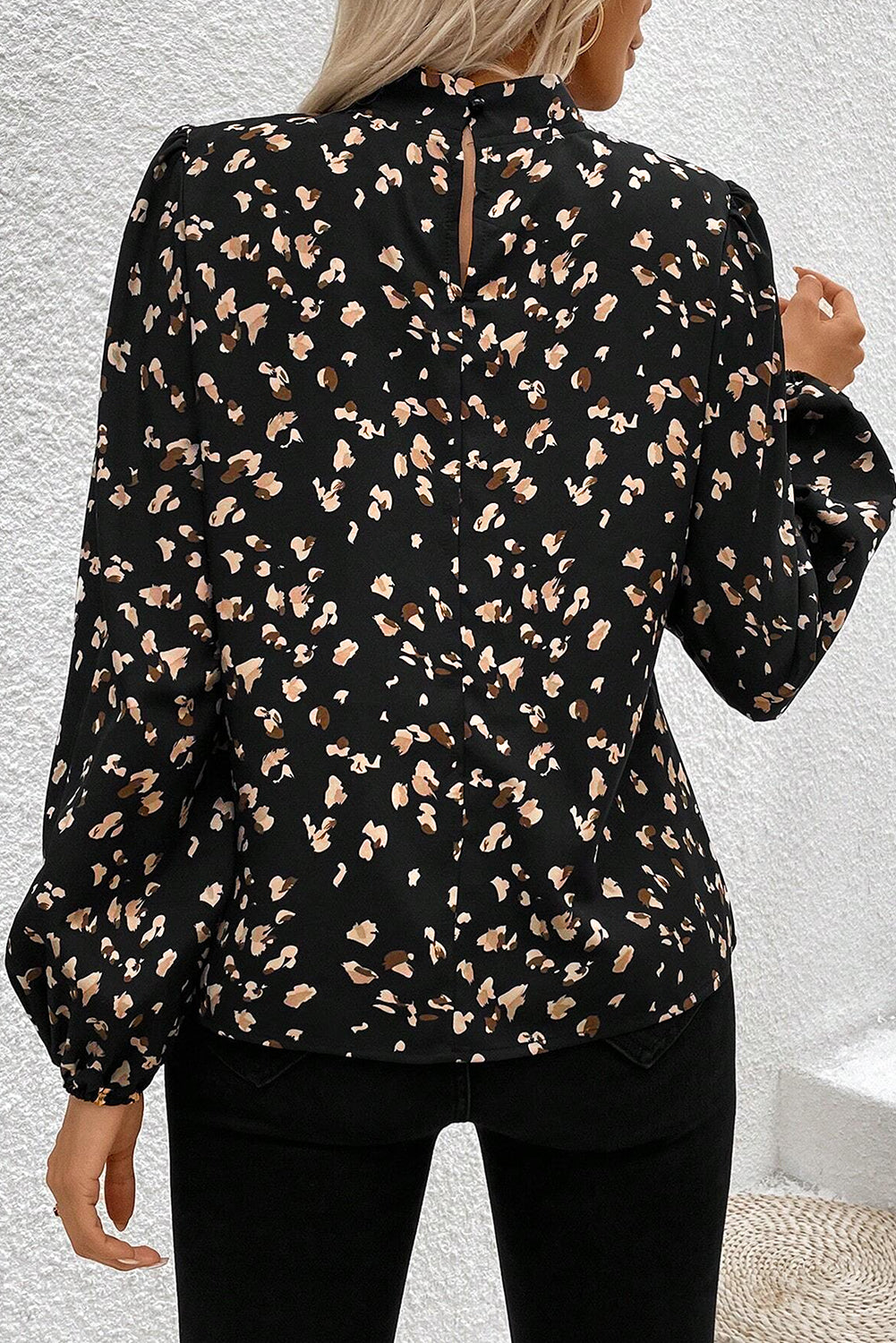 Black blouse with beige floral pattern worn by a person against a light gray background