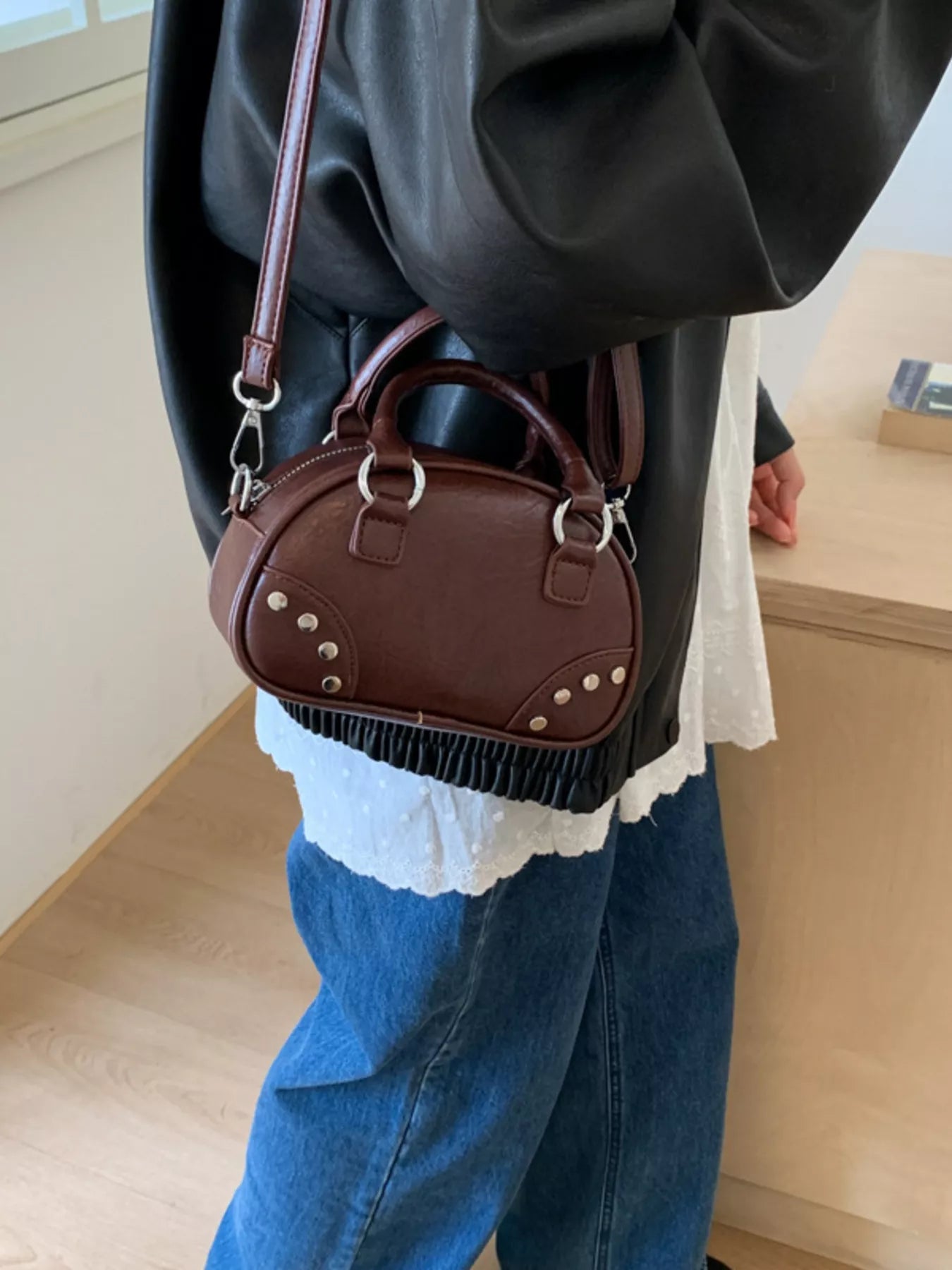 Person holding a brown handbag with a white lace top, wearing a black jacket and blue jeans.