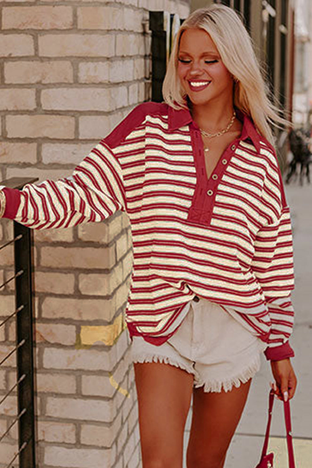 Woman wearing a red and white striped shirt standing against a brick wall.