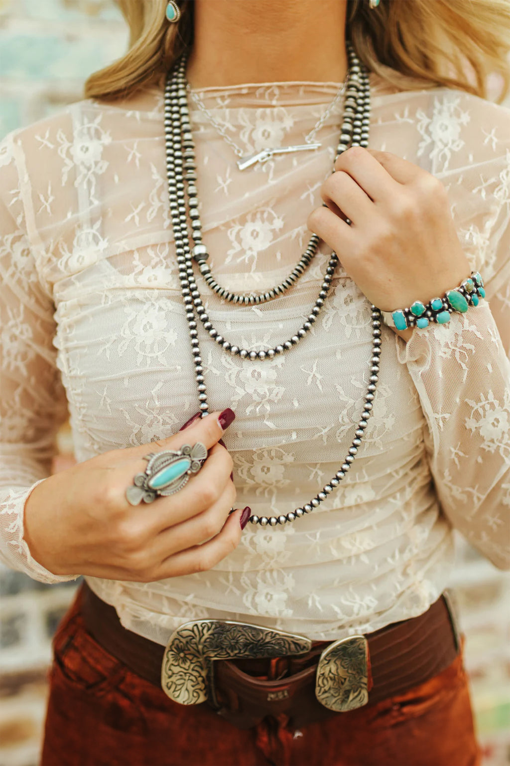 Person wearing a white lace top with layered necklaces and jewelry. Close-up