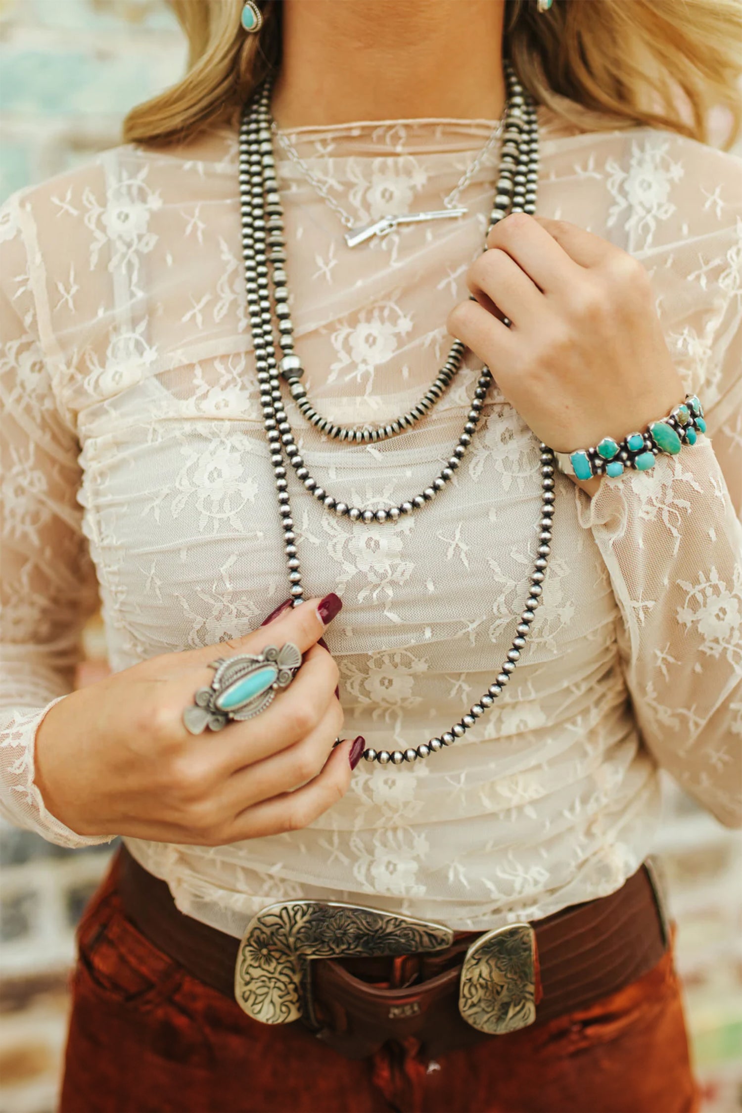 Person wearing a white lace top with layered necklaces and jewelry. Close-up
