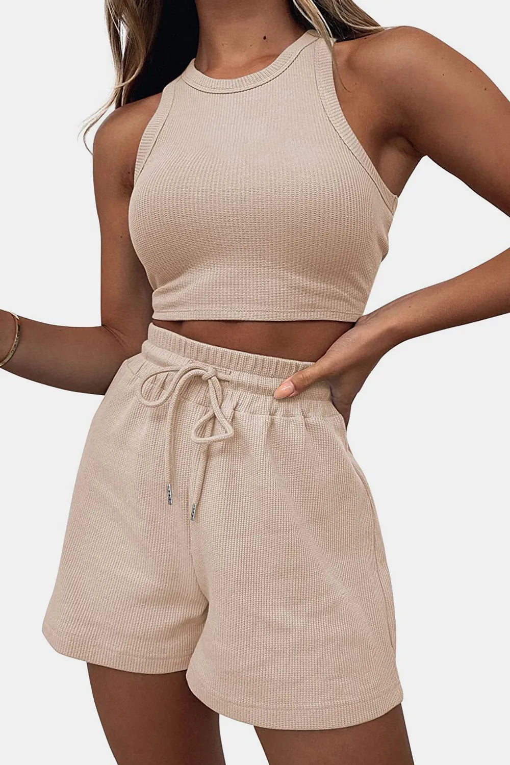 Woman wearing a beige ribbed tank top and shorts set on a plain background