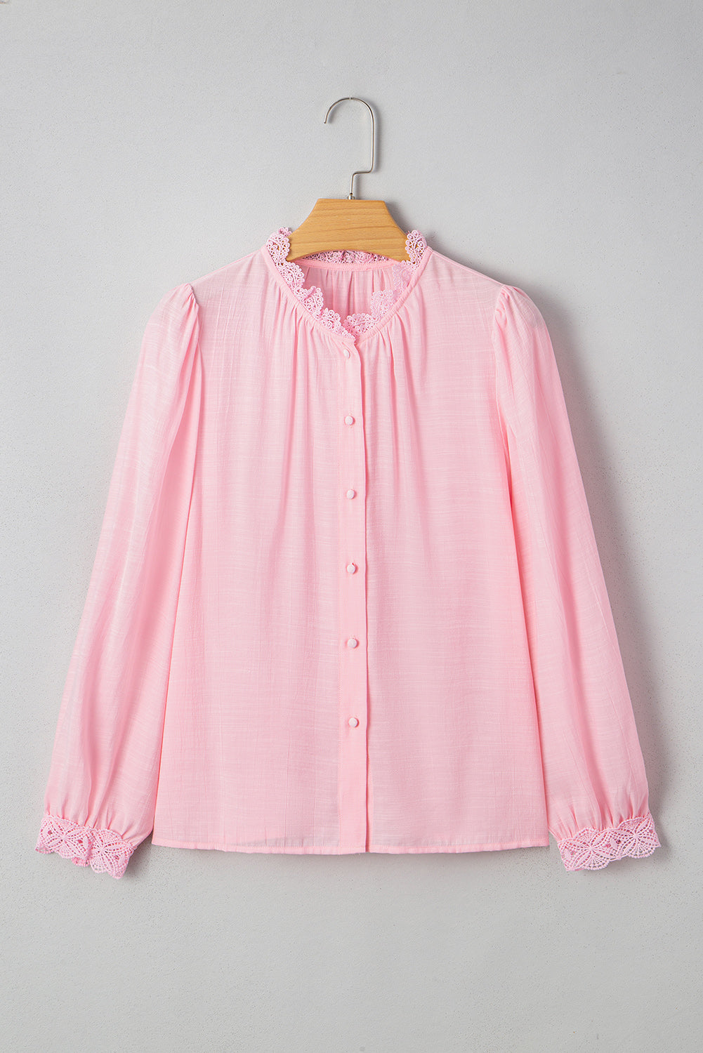 Pink blouse with lace details on a wooden hanger against a gray background