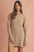 A woman modeling a chunky cable-knit sweater dress in a warm beige color.