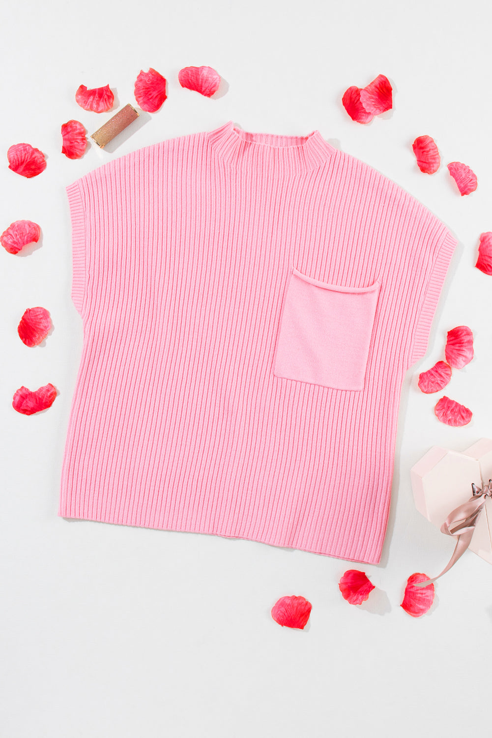 Pink ribbed sweater with a pocket on a light gray background with pink petals.