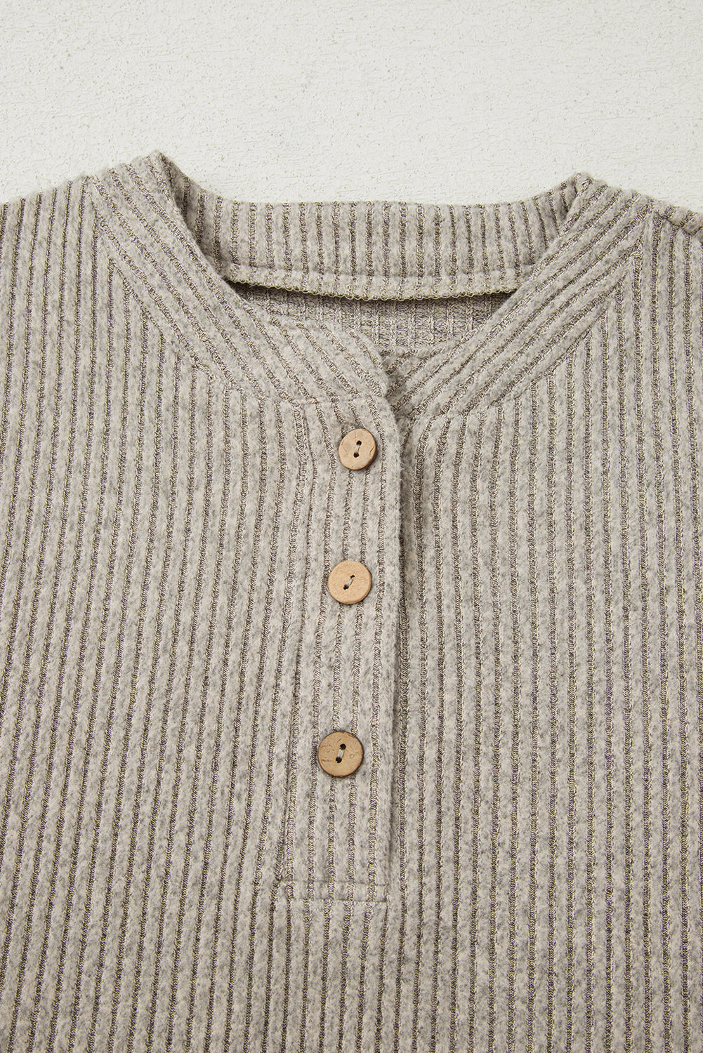 Close-up of a ribbed sweater with button details on a light background