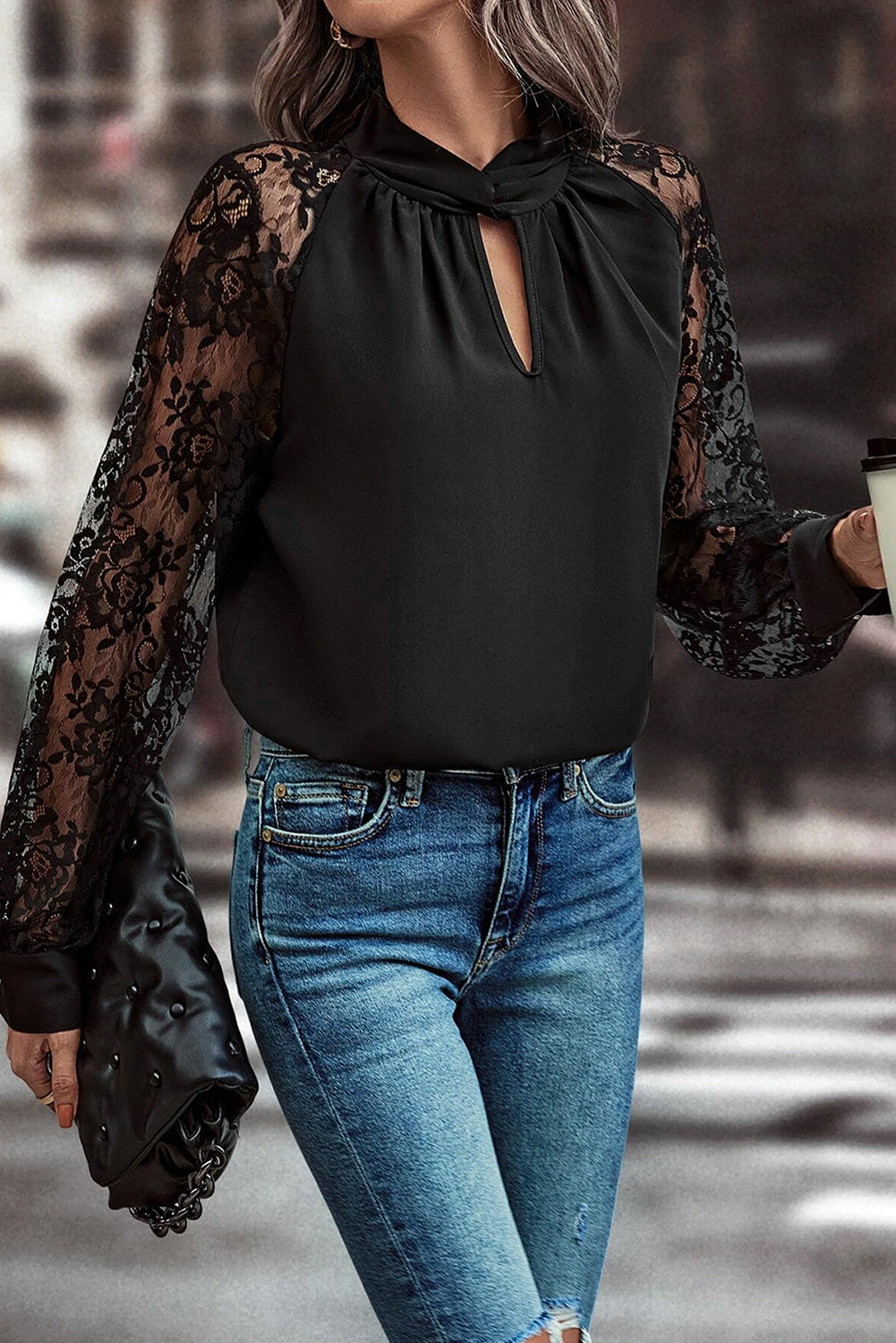 Person wearing a black top with lace sleeves and blue jeans in an urban setting