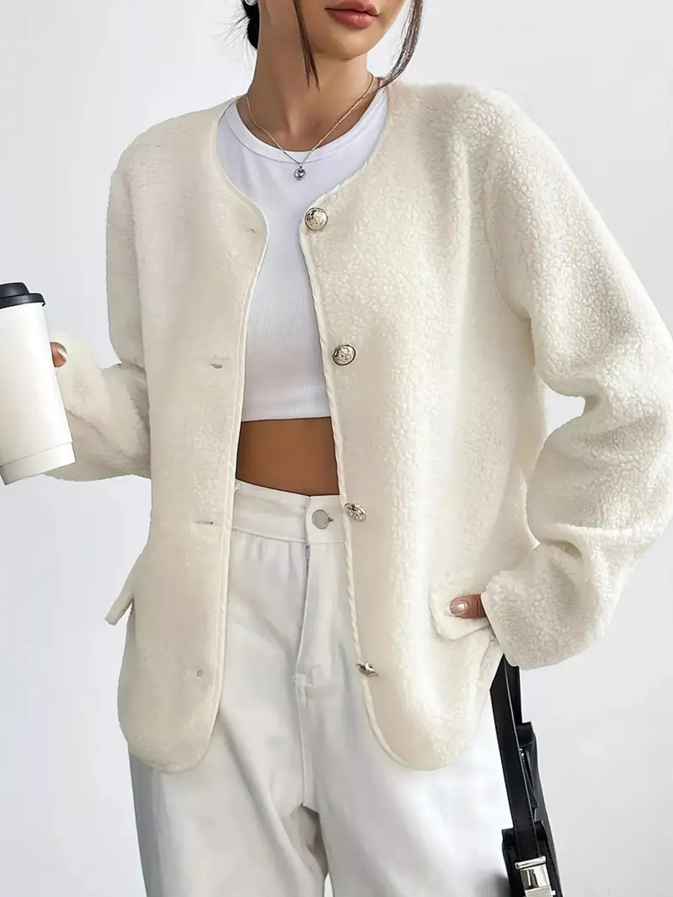 Person wearing a cream-colored cardigan over a white top and pants, holding a coffee cup.