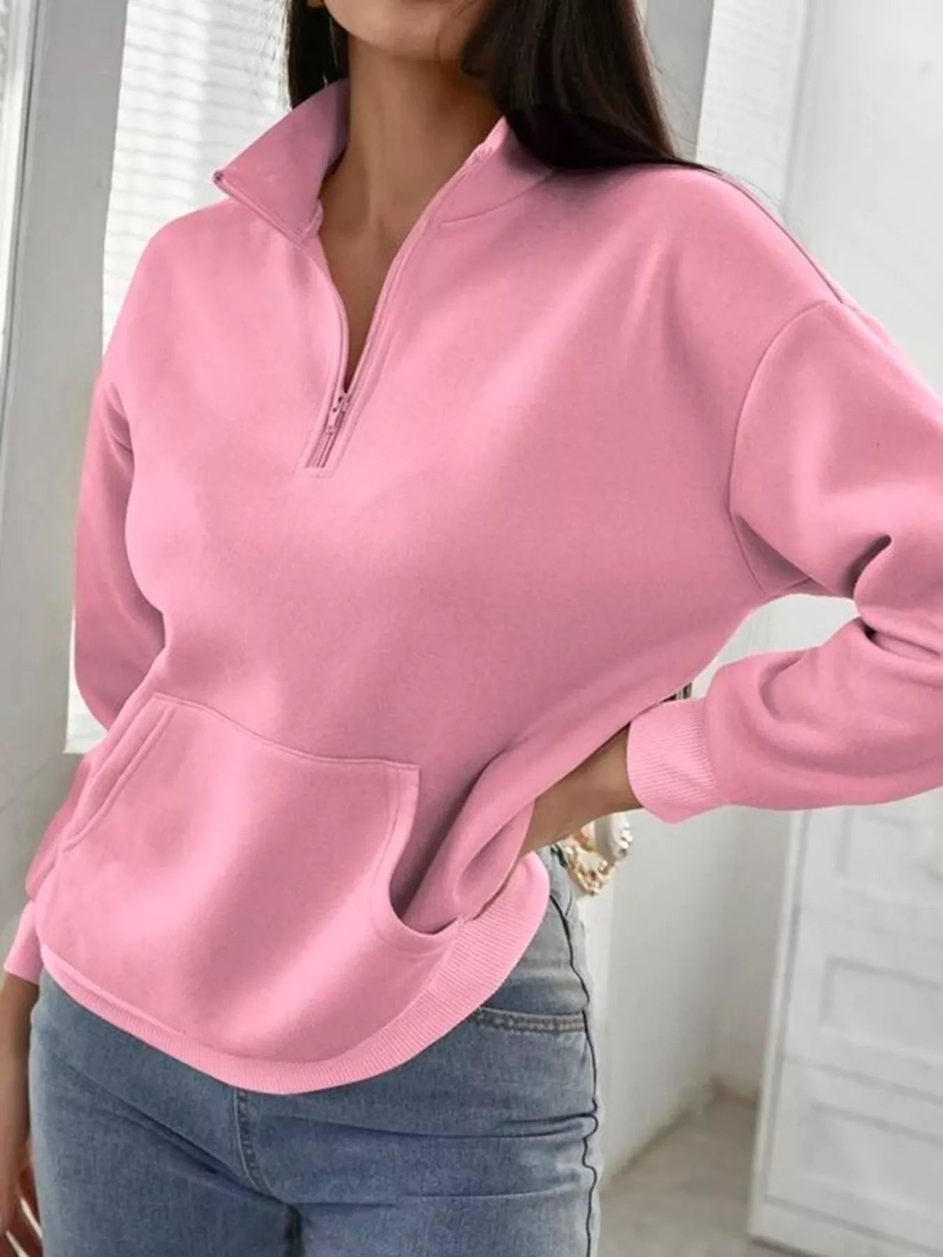 Person wearing a pink pullover with a zipper, standing indoors.