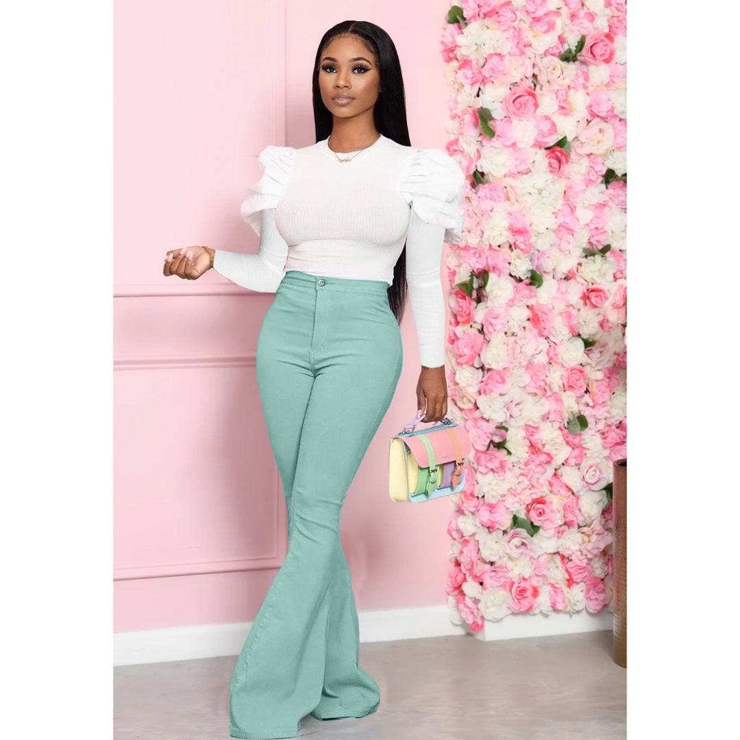 Woman in white top and green pants standing next to a pink floral wall.